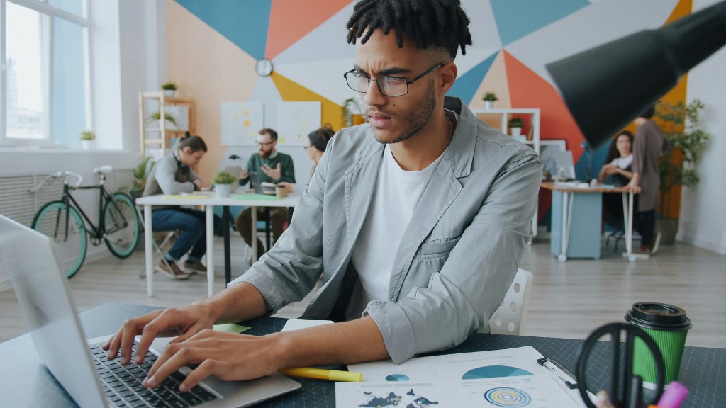 A man in glasses typing at a laptop in an open office